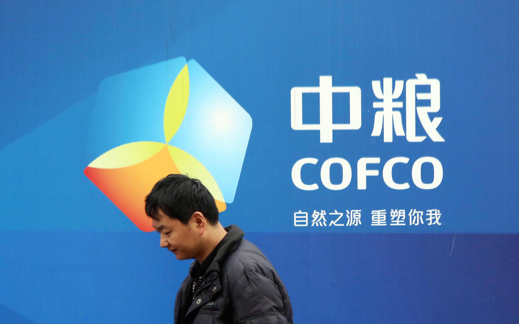 a Chinese man standing next to a Cofco poster