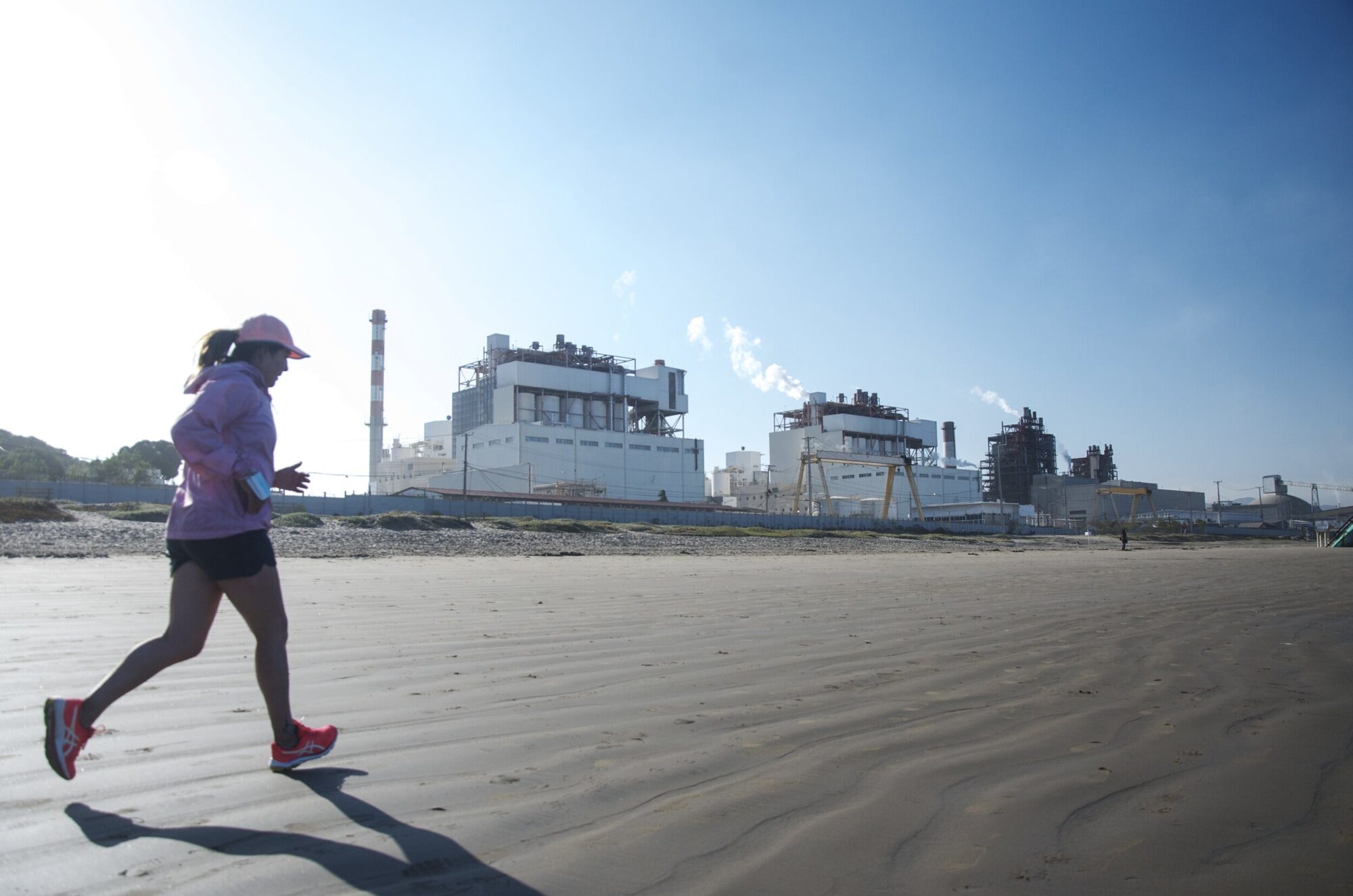 A woman runs on a beach in Chile, in front of an industrial park.