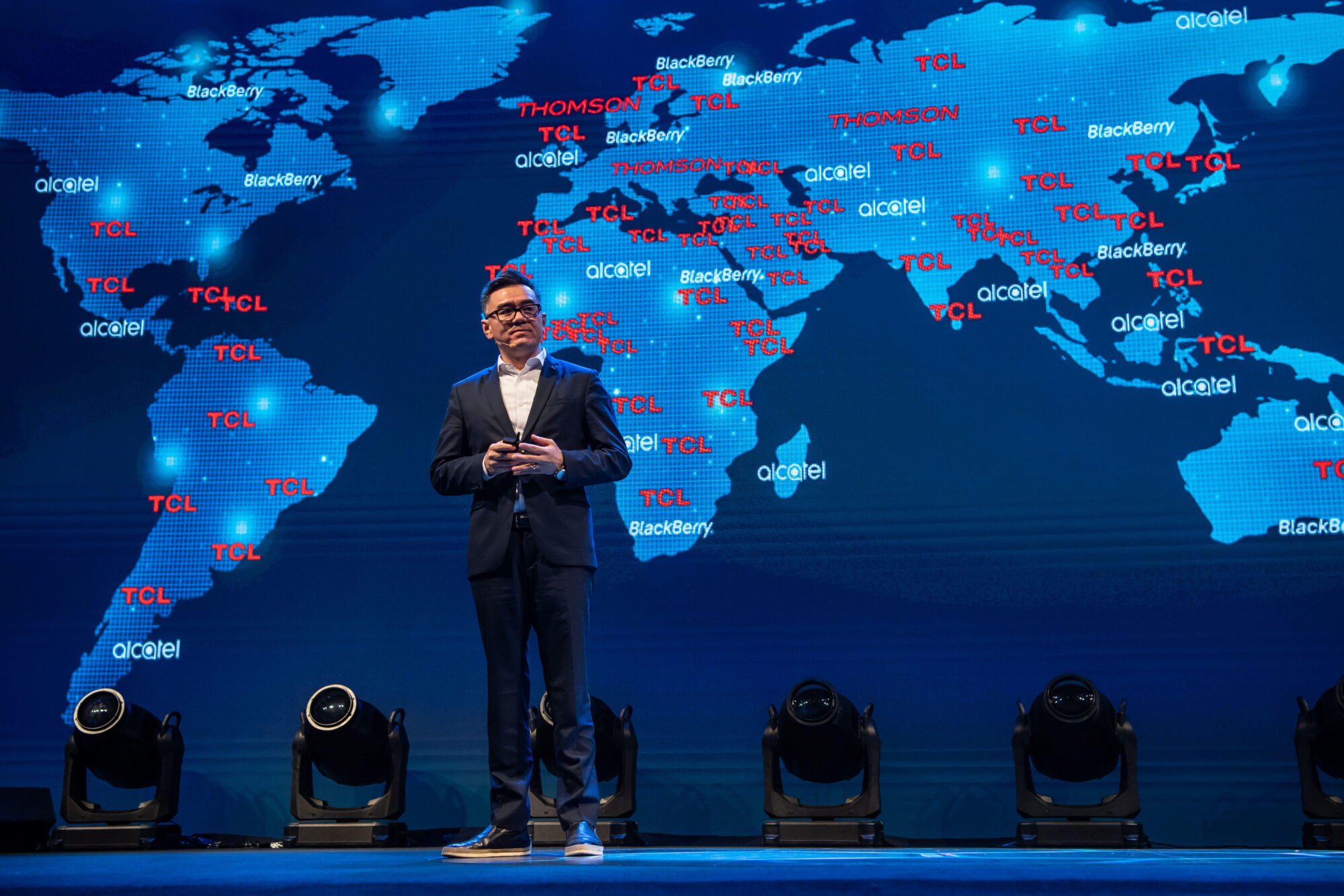 Kevin Wang Cheng, ex-CEO da TCL Multimedia Technology Holdings Limited, em um palco com um mapa do mundo atrás dele.