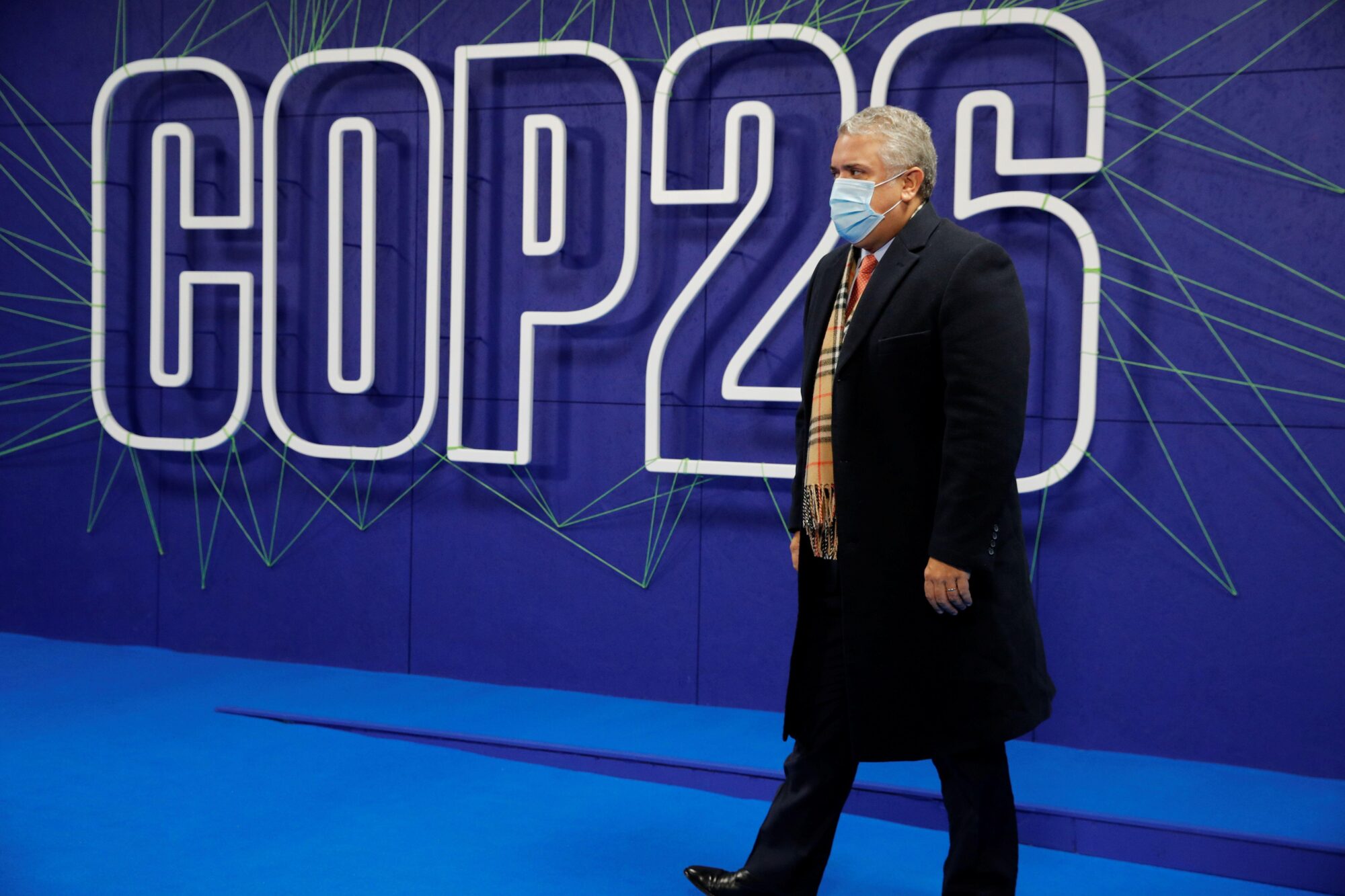 Ivan Duque camina frente a un cartel de la COP26