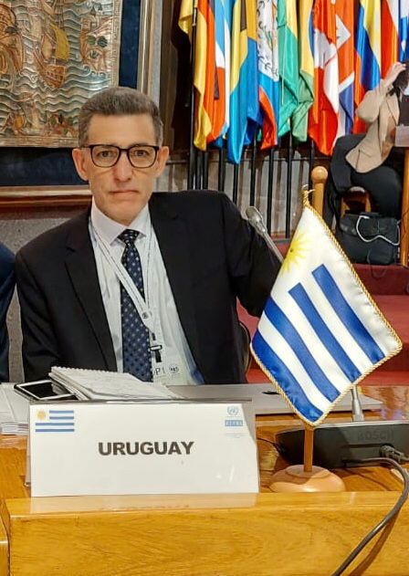 Um homem atrás de uma mesa com a bandeira do Uruguai e uma placa dizendo "Uruguay".
