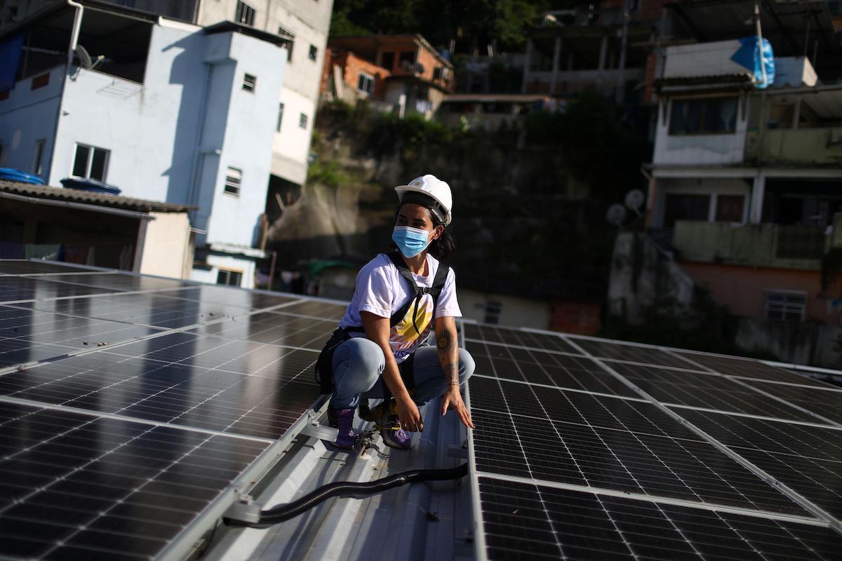 <p>Solar installer Natalia Noel Nazario checks panels on the roof of a residents’ association headquarters, fitted by NGO Revolusolar in the Babilonia favela in Rio de Janeiro, Brazil (Image: Pilar Olivares)</p>