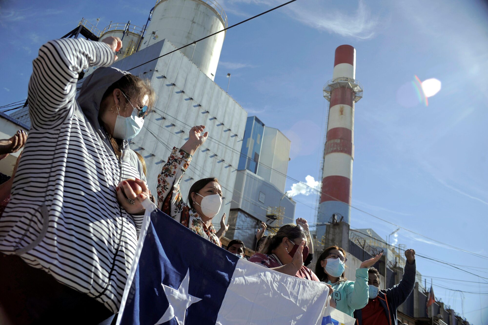 manifestantes sosteniendo una bandera chilena frente a una central termoeléctrica