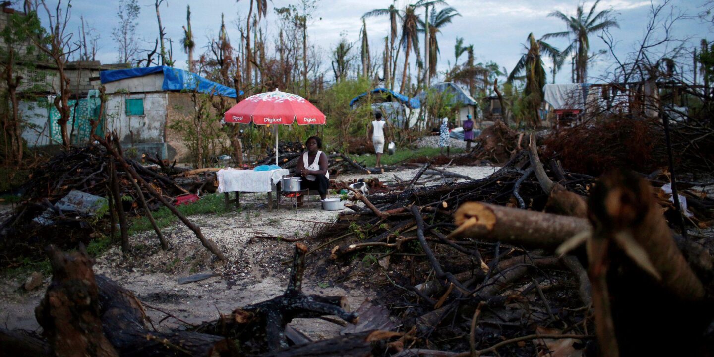 <p>Vendedora trabalha em meio a danos causados pelo furacão Matthew, no Haiti, em outubro de 2016. O financiamento por perdas e danos causados pelas mudanças climáticas tem sido a questão mais controversa da COP27 (Imagem: Carlos Garcia Rawlins / Alamy)</p>