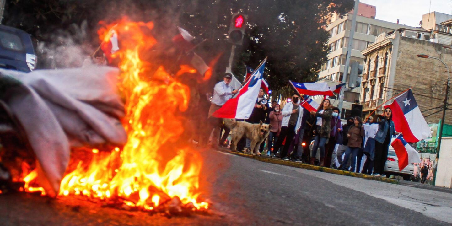 Una pancarta es incendiada mientras manifestantes sostienen banderas chilenas durante una protesta contra la nueva Constitución en Valparaíso.