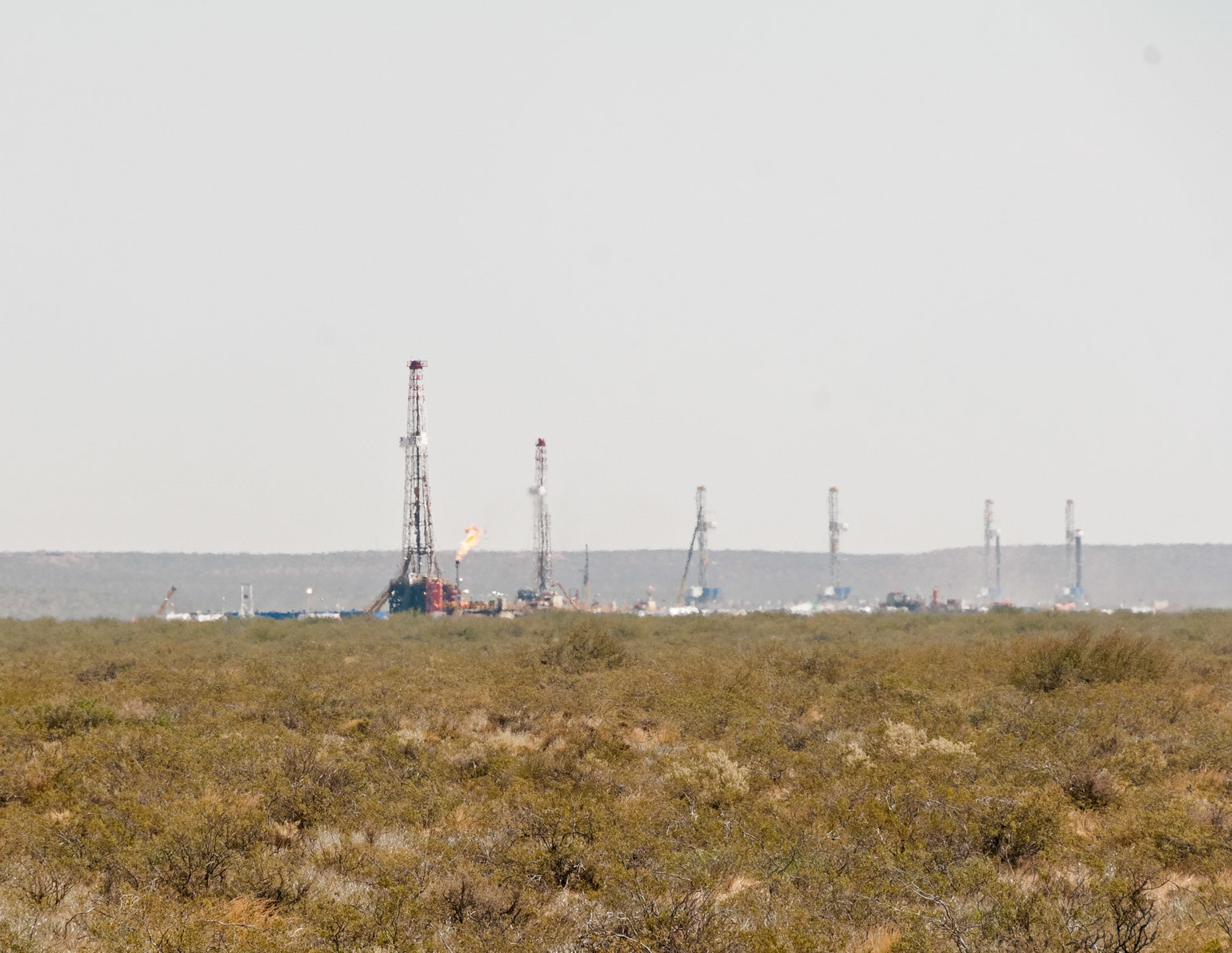 Green-yellow grassy field in front of a row of oil drills, Vaca Muerta Argentina
