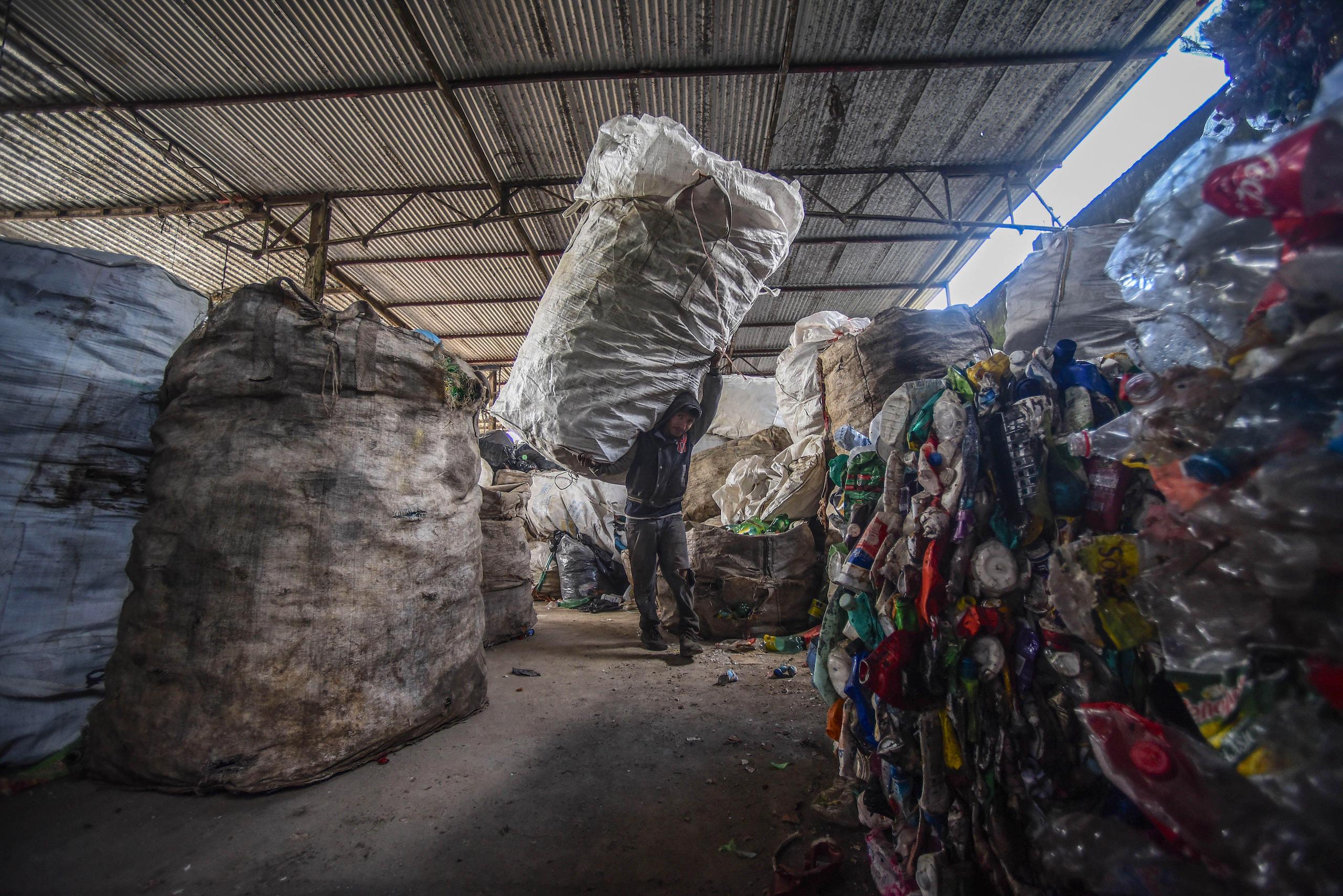 Un reciclador carga una bolsa gigante de residuos al hombro entrando en una planta de reciclaje en México.