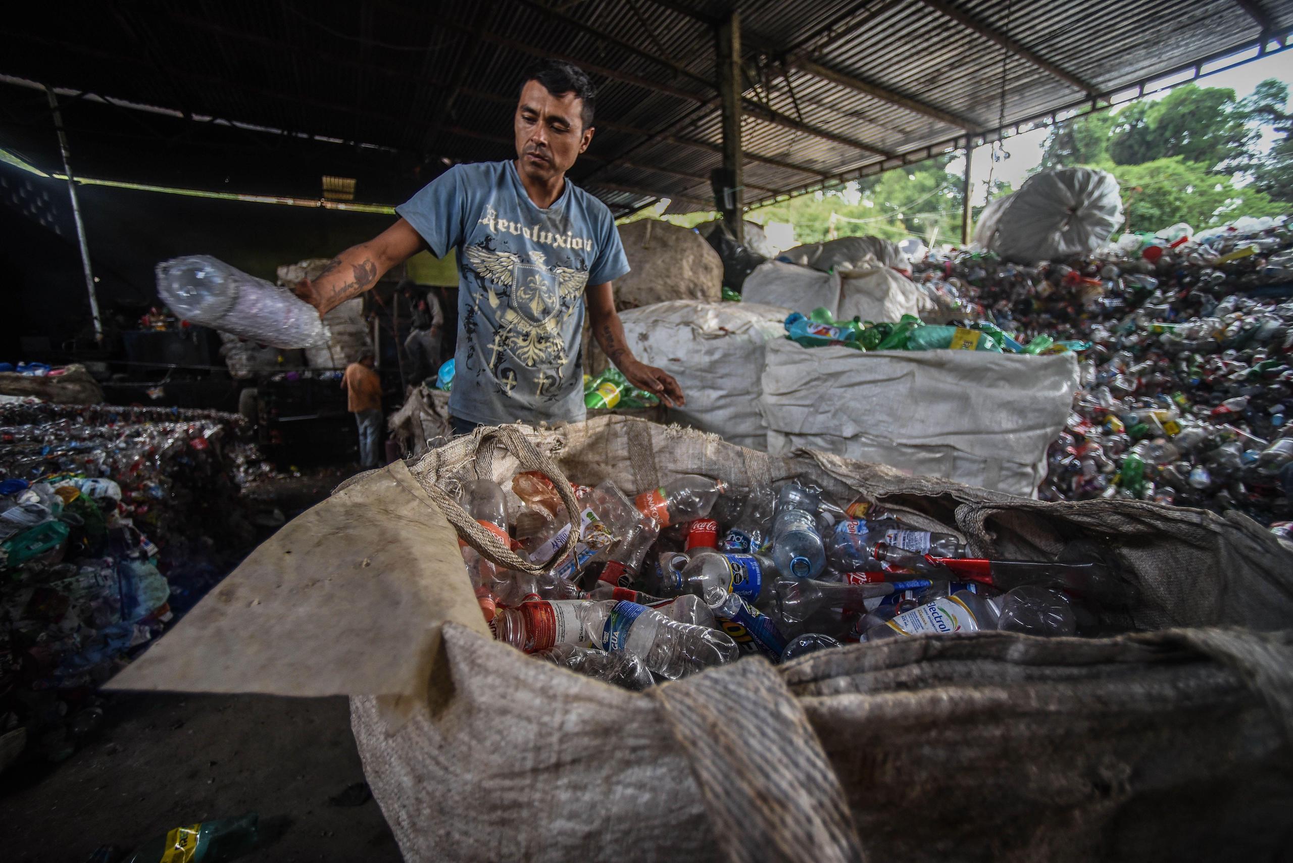 Un trabajador con una botella plástica en la mano en una planta de reciclaje