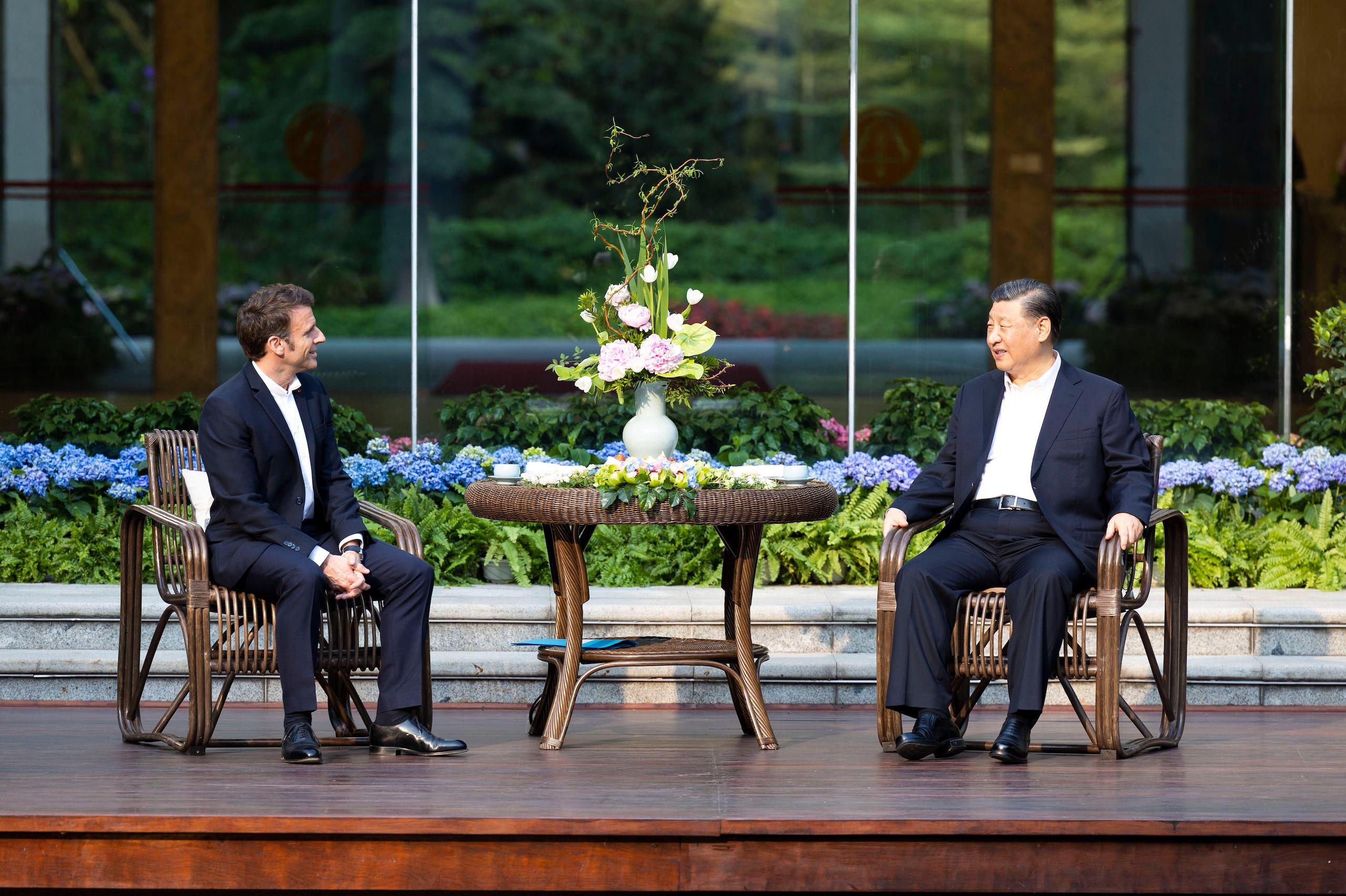 Xi Jinping e Emmanuel Macron sentados em ambos os lados de uma pequena mesa
