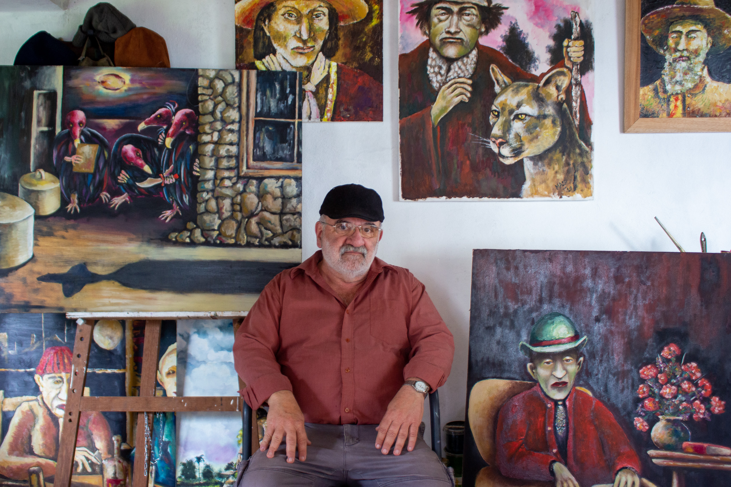 Miguel Ángel Olivera Prieto sits in his art studio at home in Tambores, with six painted portraits hung behind him