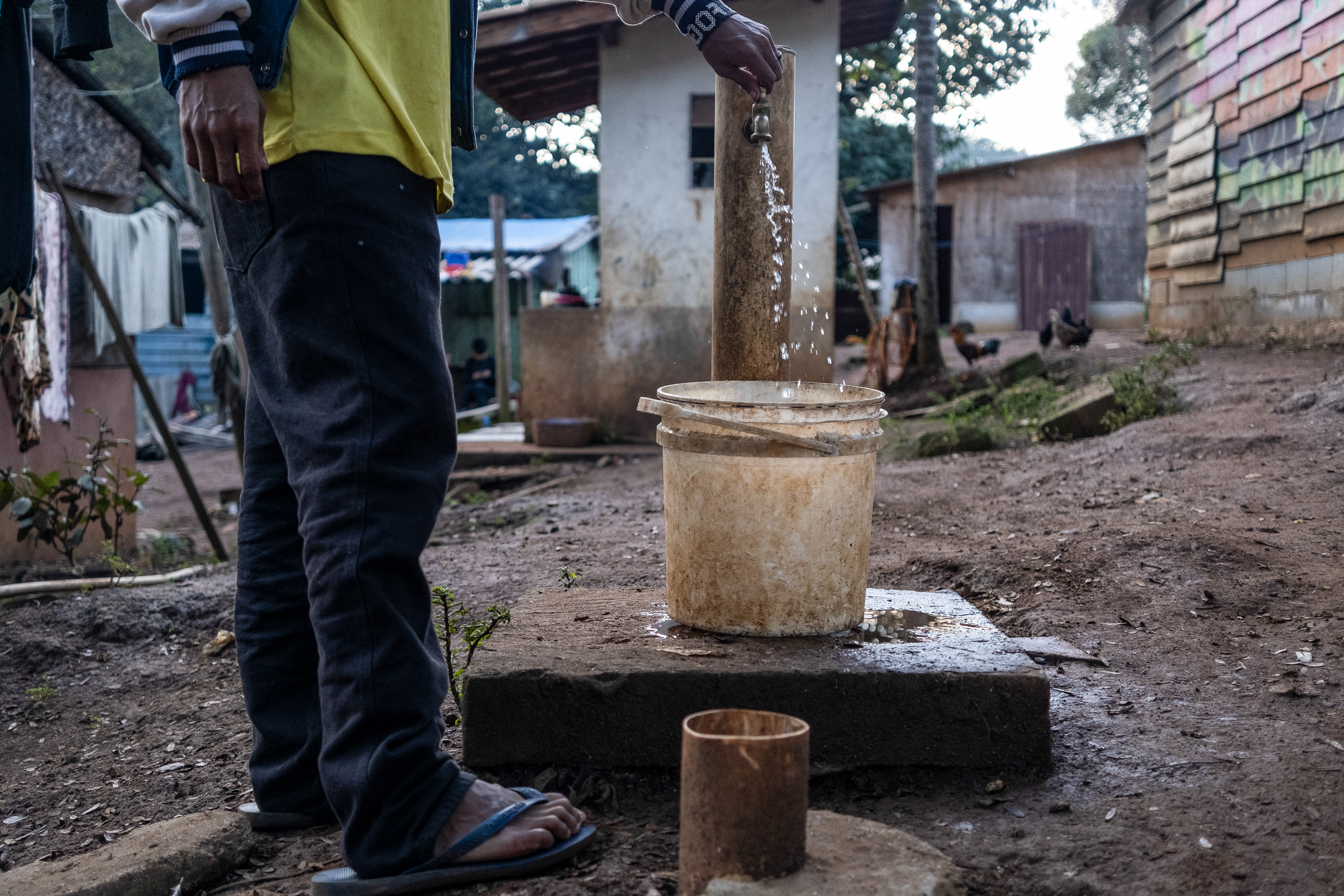 Morador da aldeia enche um balde d’água para tomar banho
