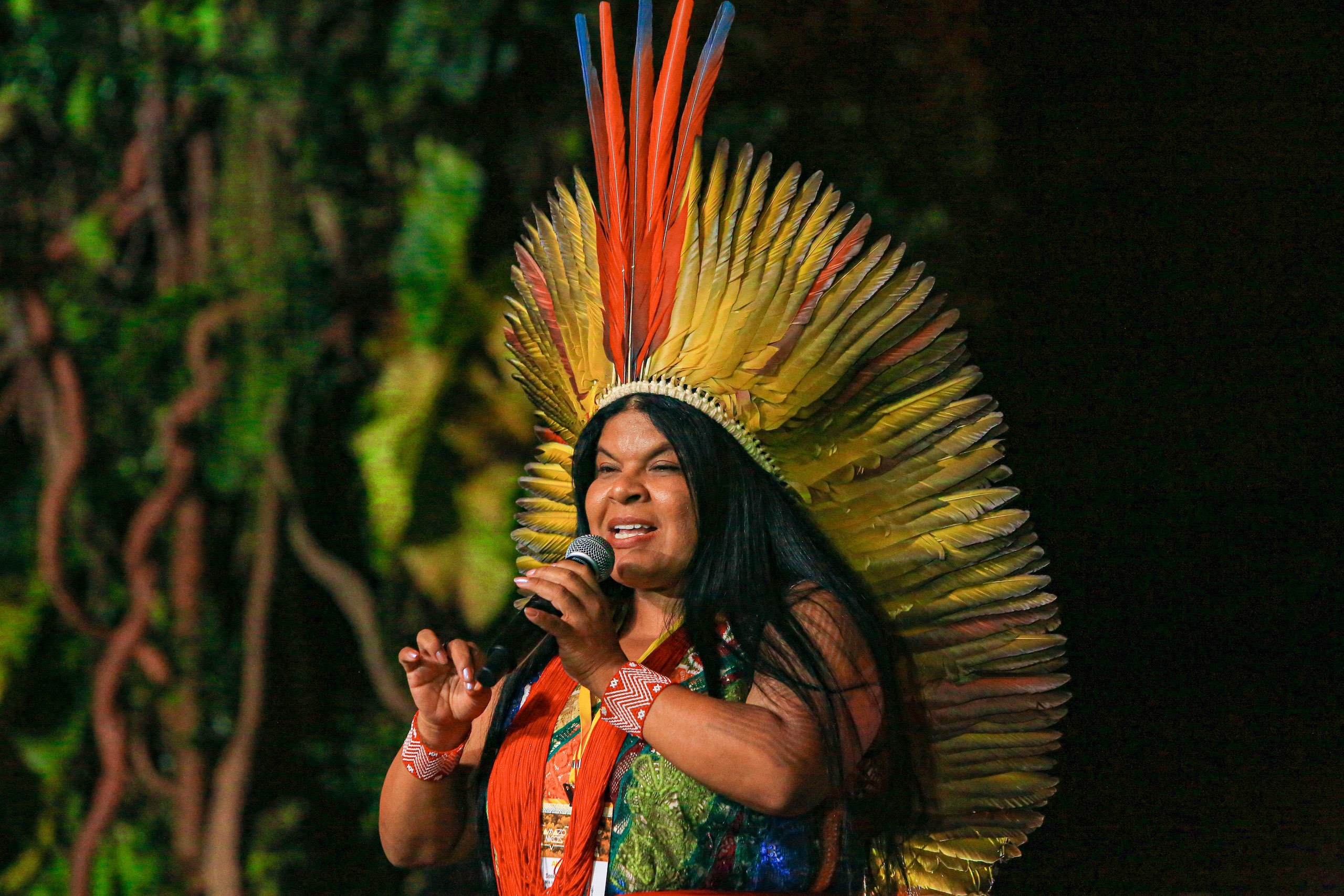 Sonia Guajajara habla con un micrófono en la mano, vestida con un traje tradicional indígena