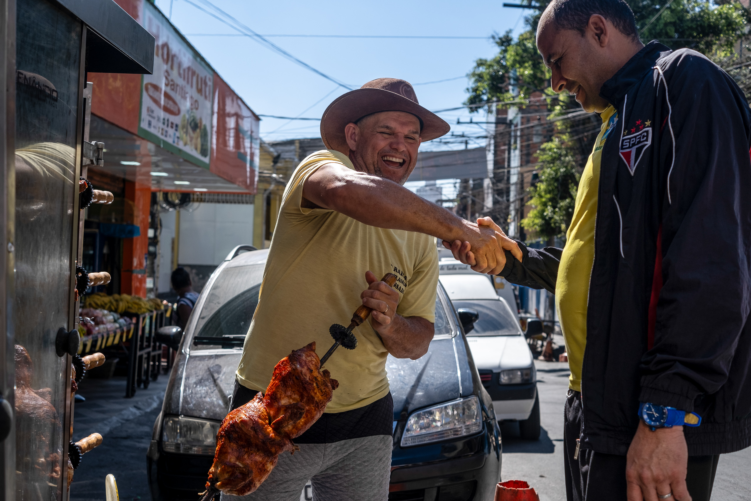 un hombre que sujeta un pincho con un trozo de carne y saluda a otra persona