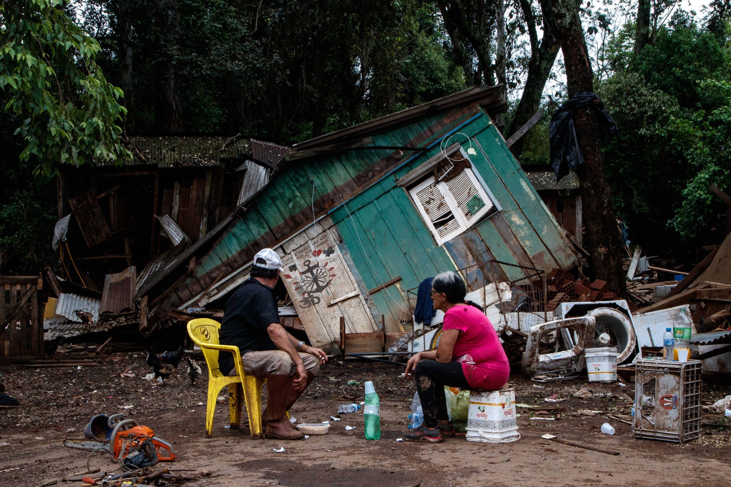 People sit in front of a cabin destroyed by floods