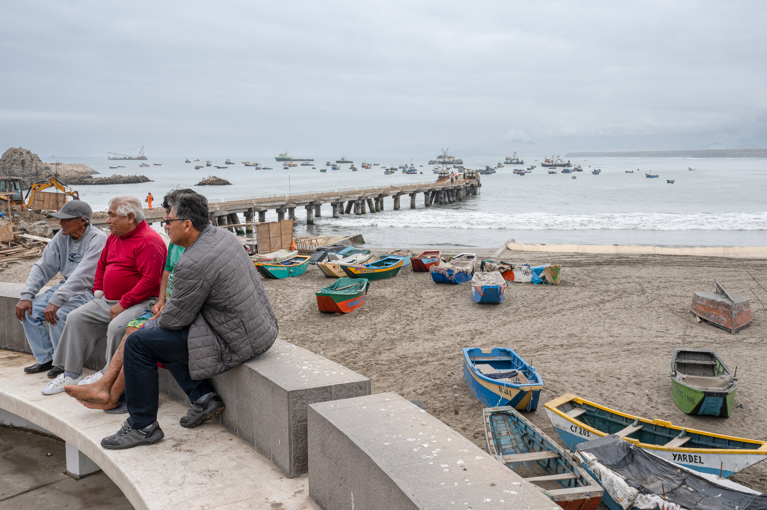 grupo de hombres sentados en una estructura de hormigón en la playa 