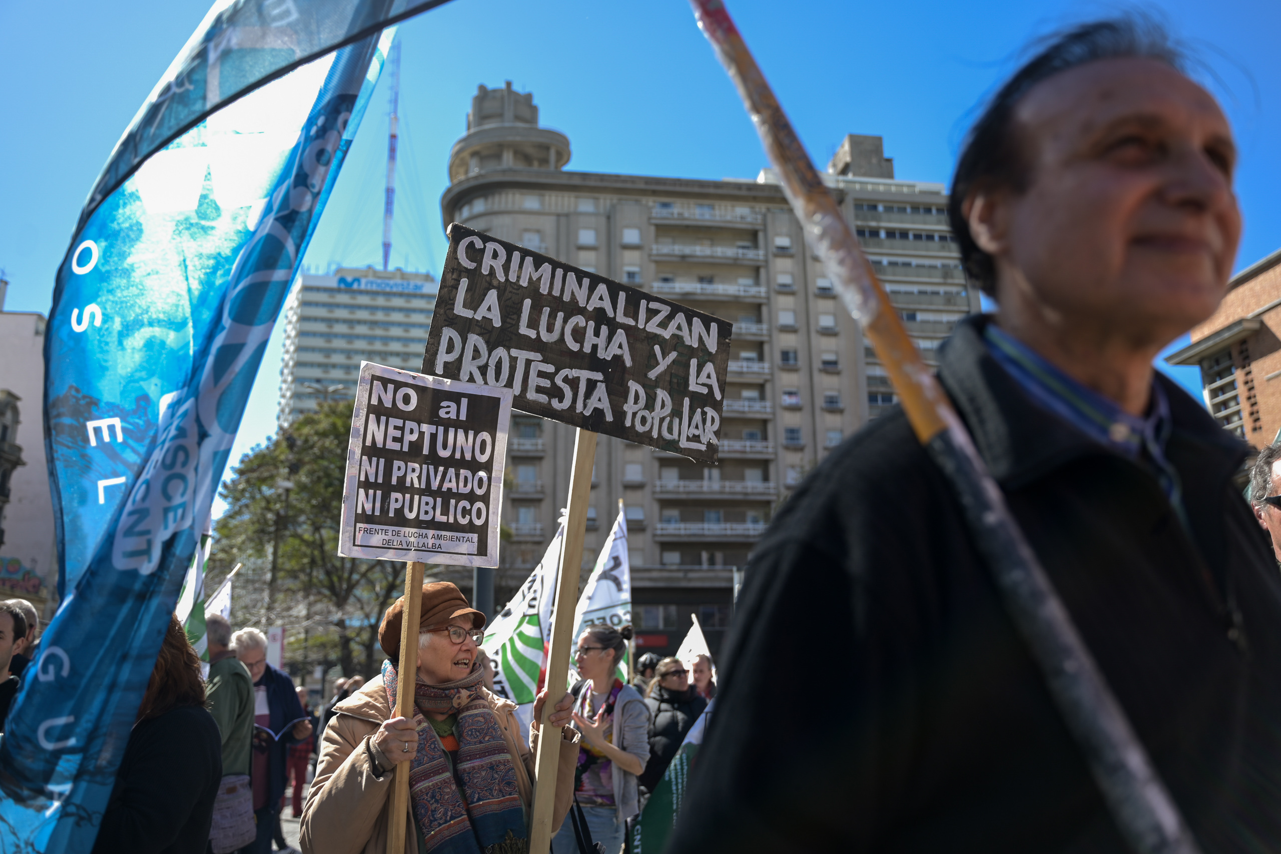 personas en una protesta con carteles que dicen "no al Neptuno ni público ni privado" y "Criminalizan la lucha y la protesta popular"