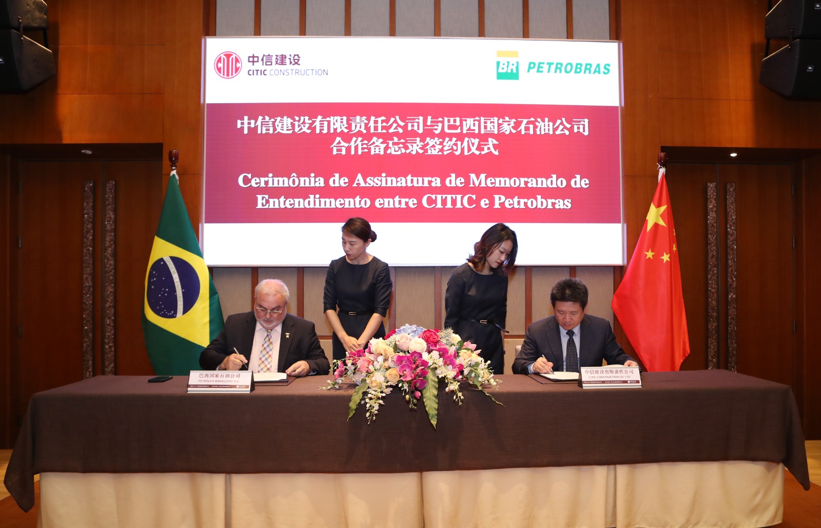 Four people at a table, between Brasil and China flags signing documents,