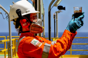 Una trabajadora vestida con un mameluco anaranjado sosteniendo un tarro de petróleo
