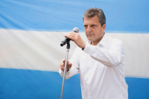 Sergio Massa standing behind a microphone in front of a large Argentina flag