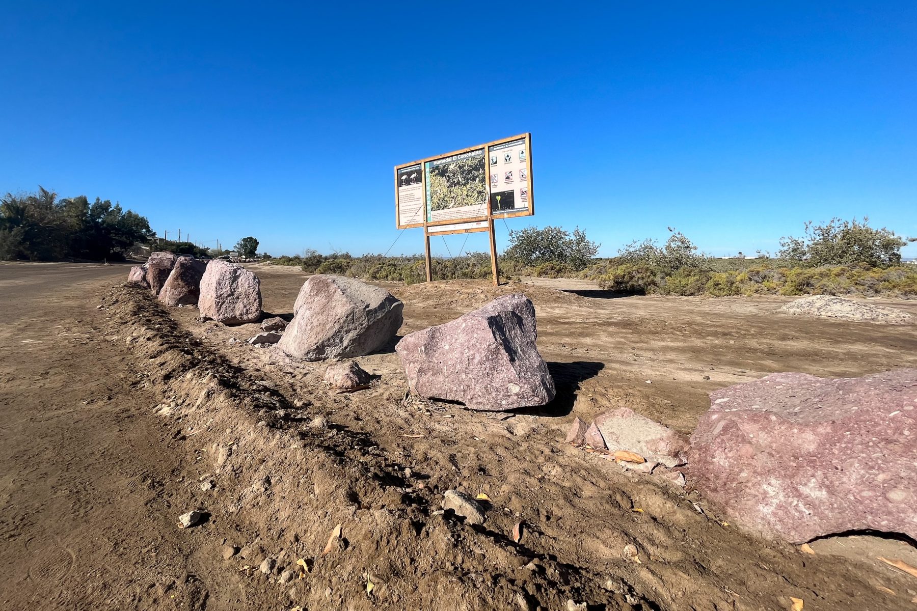 A line of boulders on dirt ground, bright blue sky