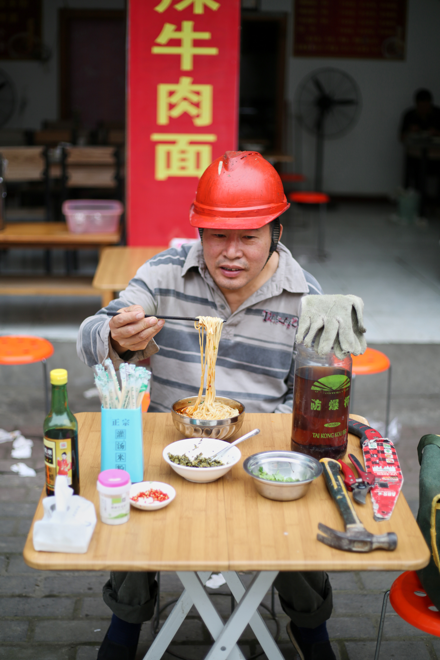 Man wearing a hardhat eating noodles with chopsticks