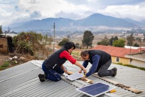 two people installing solar panels on a house roof
