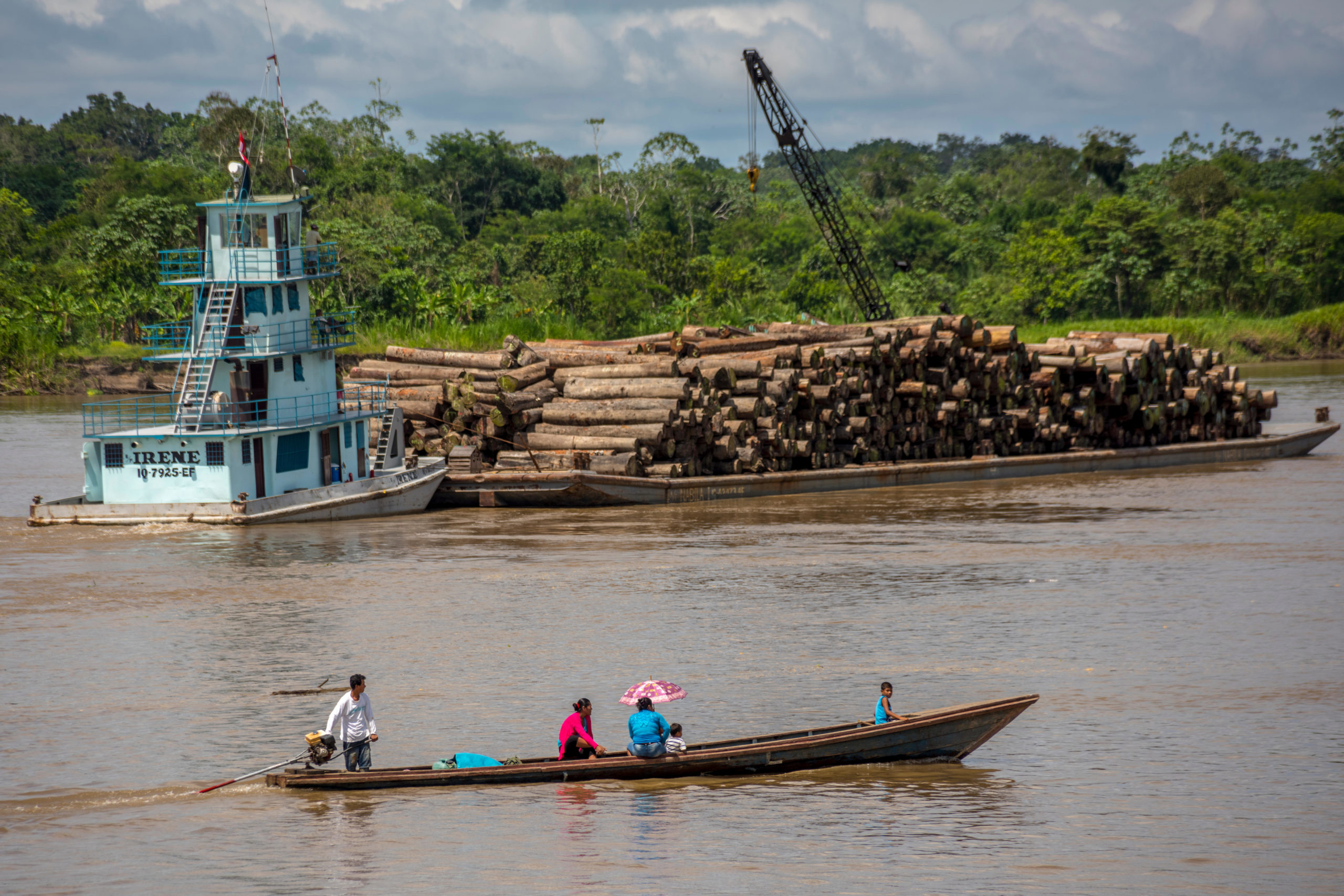 people in small boat watching larger vessel carting timber on river