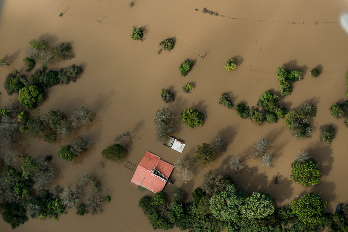 Overhead view of flood water surrounding small building and forested area